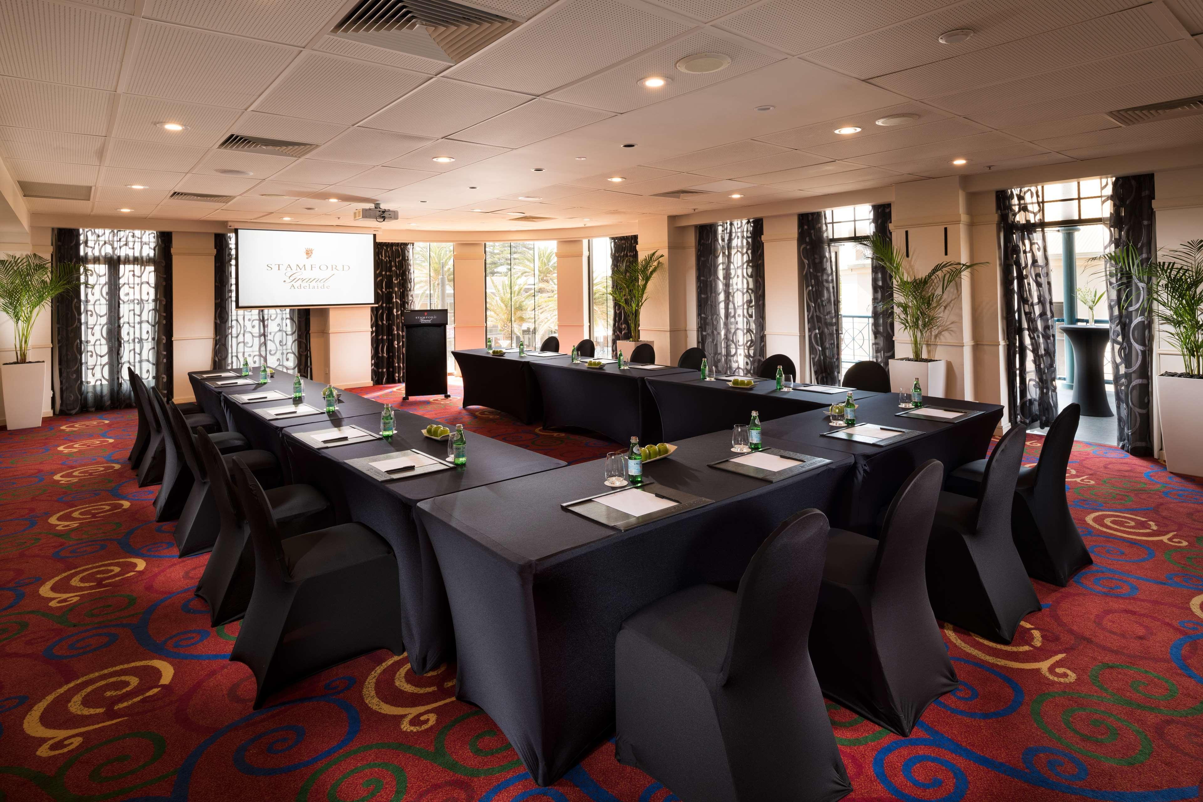 Stamford Grand Adelaide Otel Glenelg Dış mekan fotoğraf The photo shows a conference room set up for a meeting or presentation. There are several tables arranged in a U-shape, covered with black tablecloths. Each table has a notepad and a small bottle of water on it. The chairs around the tables are also 