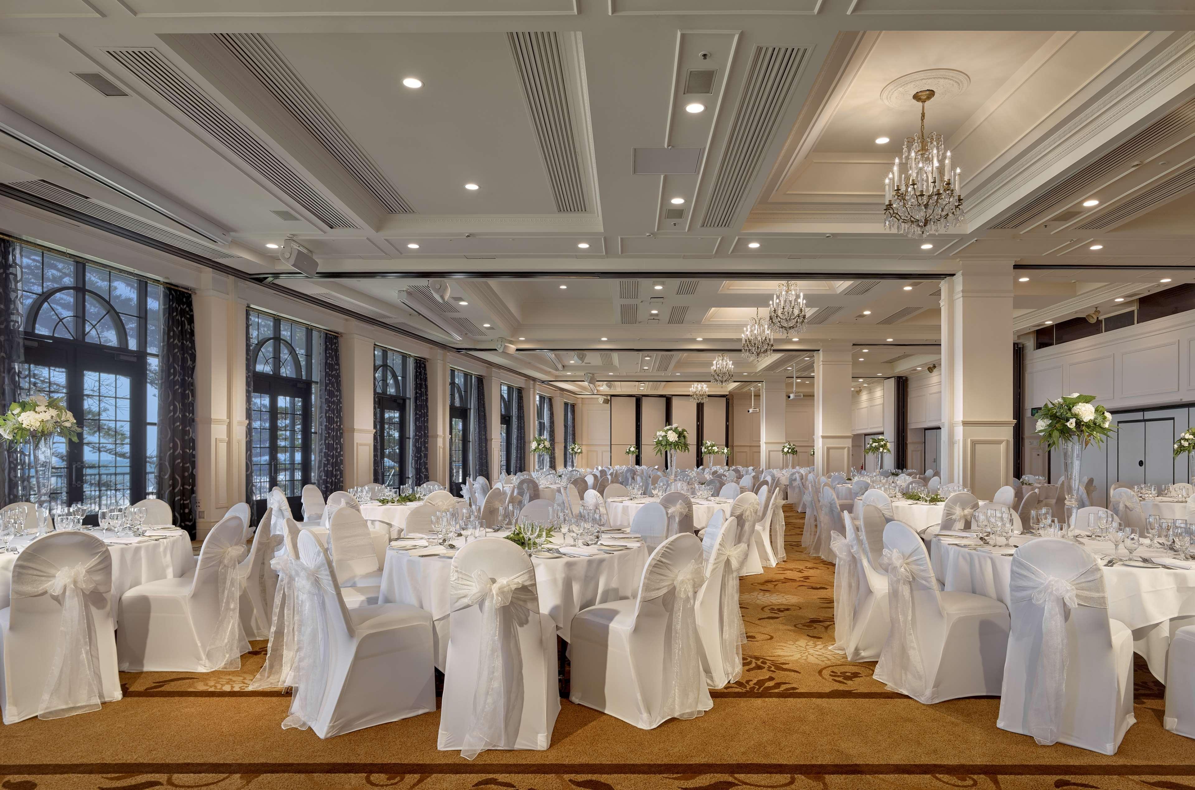 Stamford Grand Adelaide Otel Glenelg Dış mekan fotoğraf The photo depicts an elegantly arranged banquet hall or dining area. The space features multiple round tables, each set with white tablecloths and decorated with floral centerpieces. The chairs are covered in white fabric, contributing to a formal at