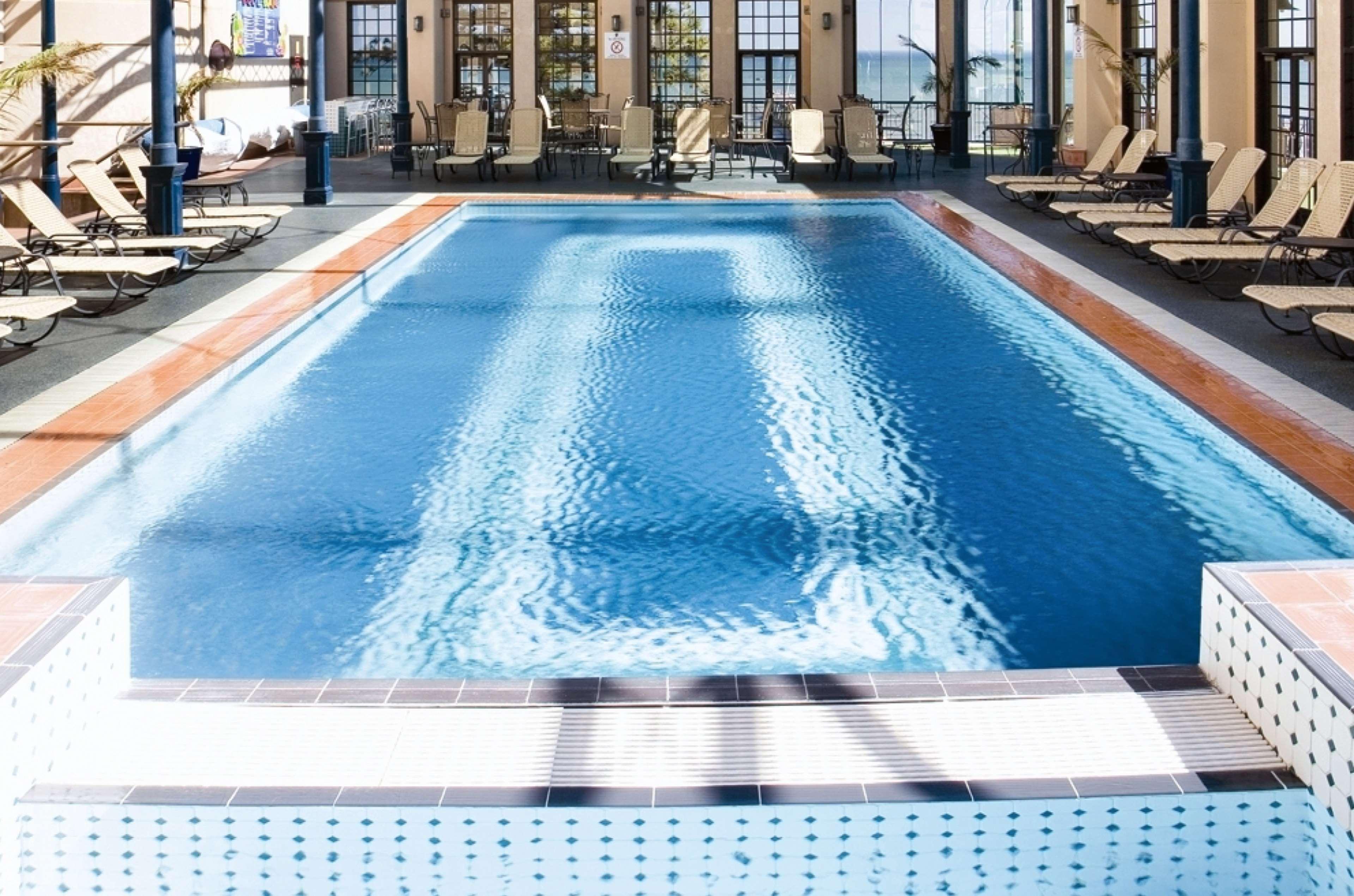 Stamford Grand Adelaide Otel Glenelg Dış mekan fotoğraf The photo shows an indoor swimming pool with a pristine blue surface. The pool is surrounded by a tiled deck and has lounge chairs lined up along the sides. Large windows allow natural light to flood the area, creating a bright and inviting atmospher