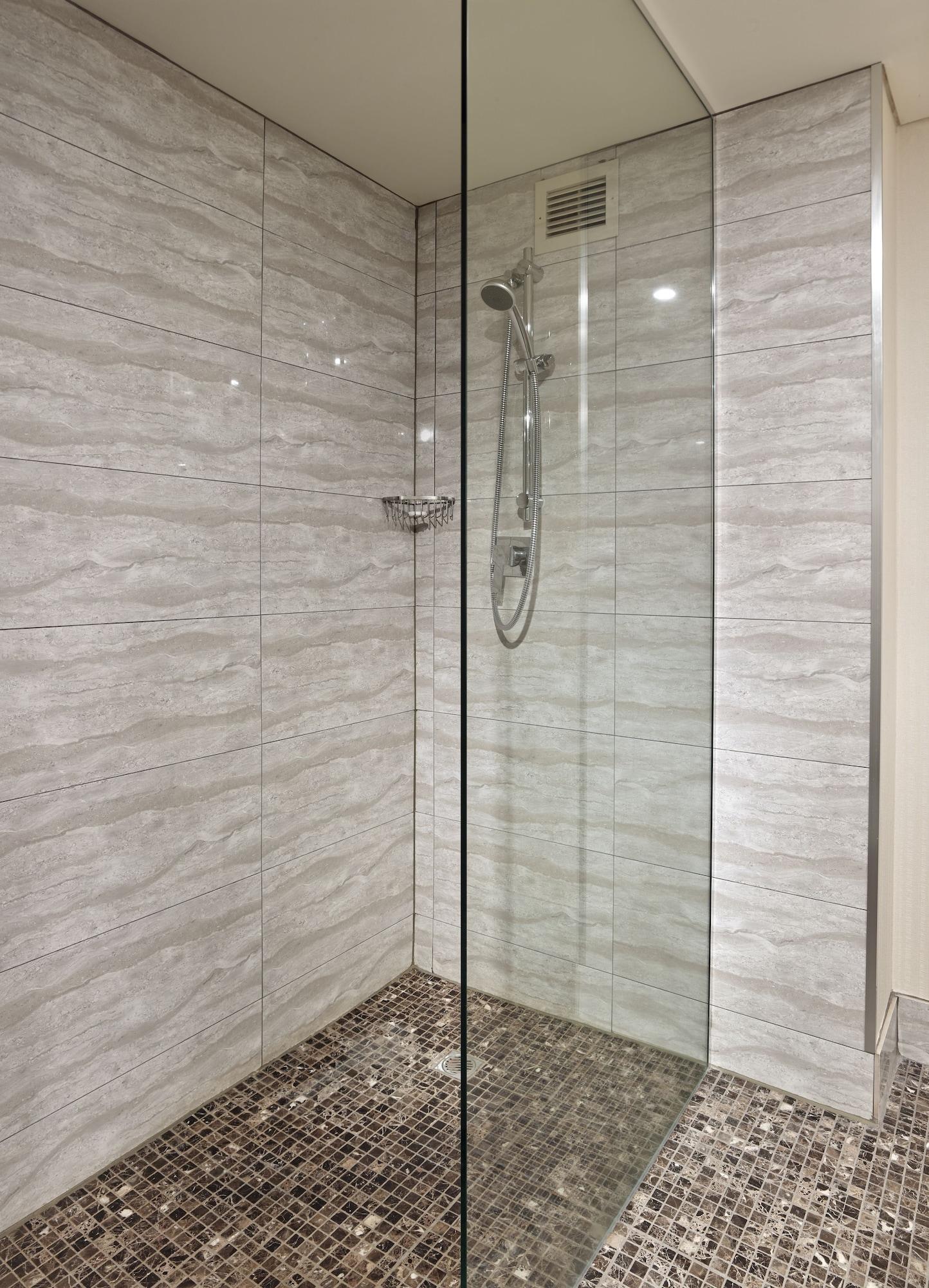 Stamford Grand Adelaide Otel Glenelg Dış mekan fotoğraf The photo shows a modern shower enclosure with a transparent glass door. The interior features tiled walls in a light, marble-like pattern, creating a clean and sleek look. There is a showerhead mounted on the wall, and the floor appears to be tiled 