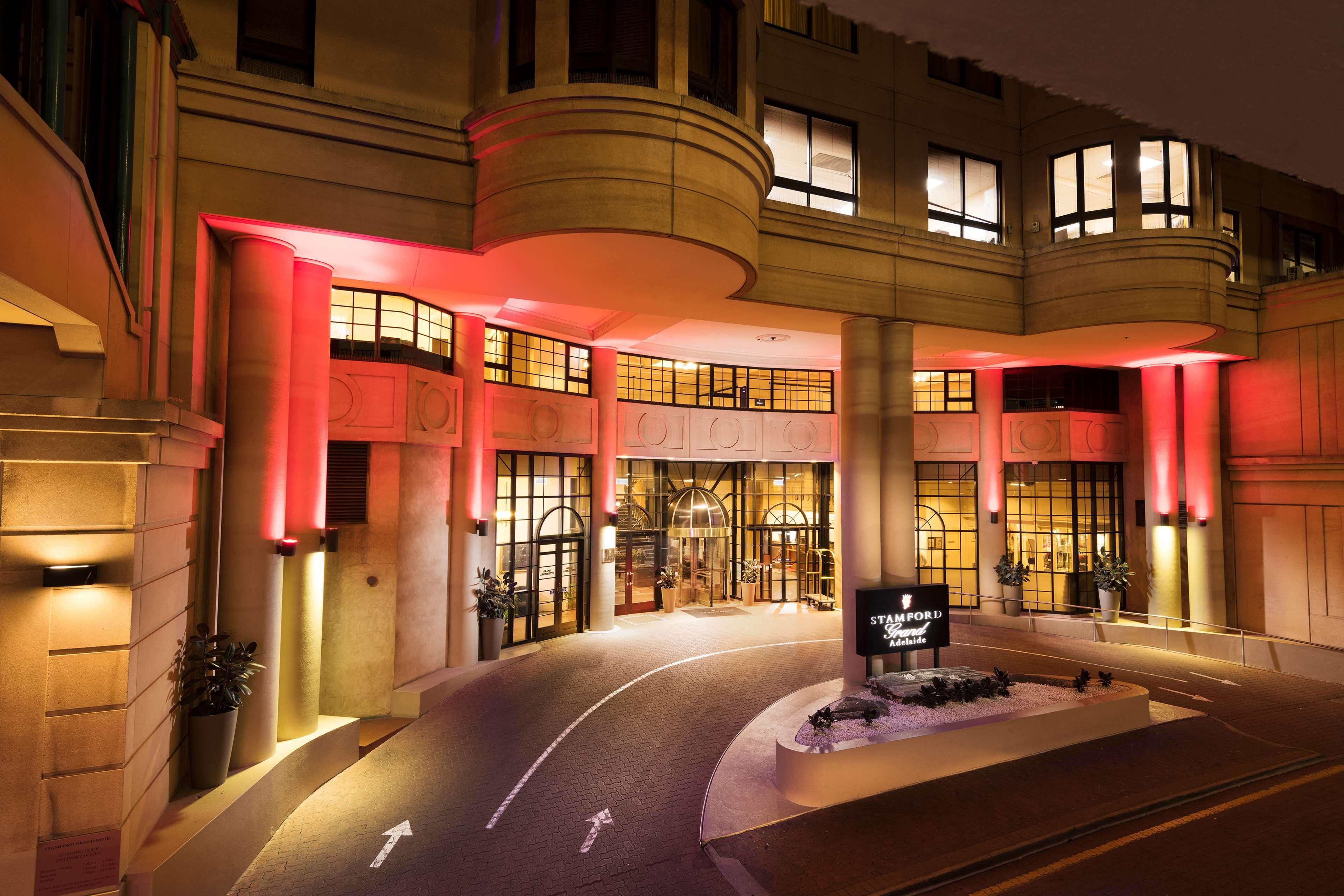 Stamford Grand Adelaide Otel Glenelg Dış mekan fotoğraf The photo shows the entrance of a hotel or luxury building at night. The façade features a modern architectural style with large windows and an elegant entrance. The area is illuminated with red lighting, creating an inviting atmosphere. There appear