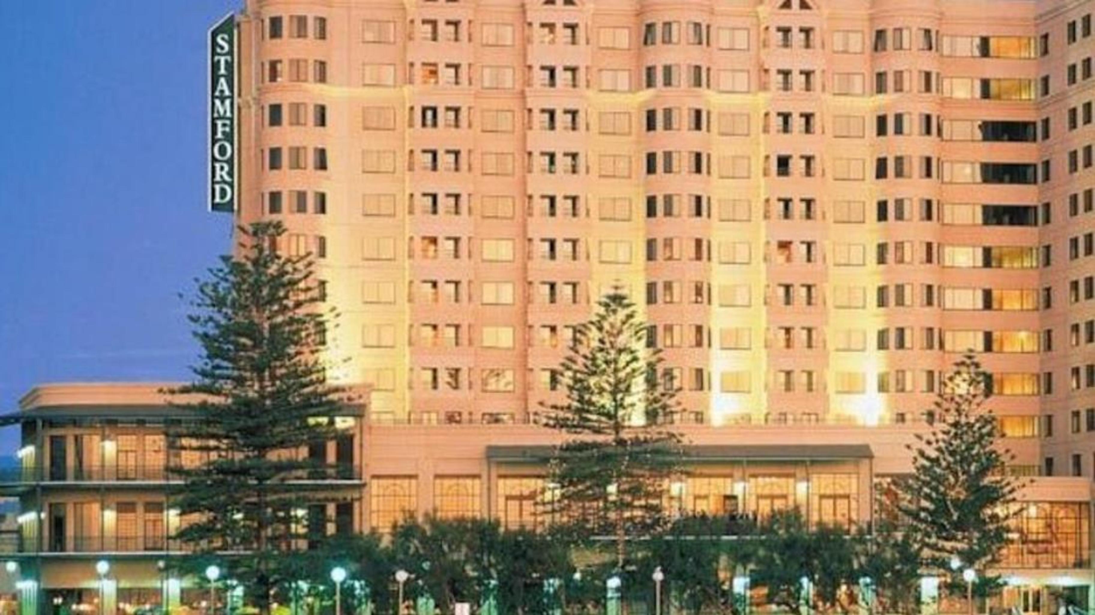 Stamford Grand Adelaide Otel Glenelg Dış mekan fotoğraf The photo shows a tall, modern building illuminated at night, likely a hotel, with the name "Stamford" prominently displayed on its side. Surrounding the building are several palm trees and landscaped areas, suggesting a tropical or coastal location.