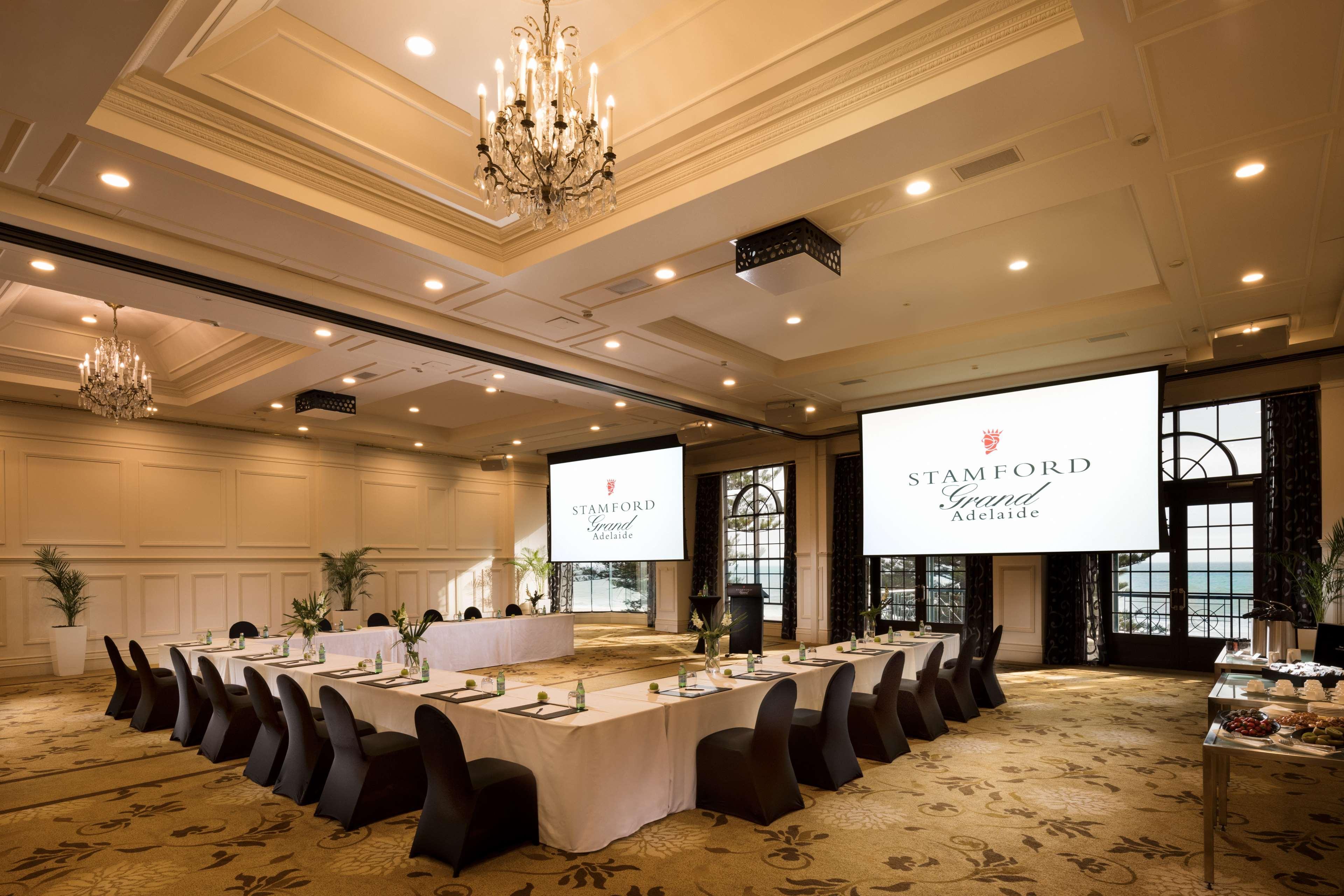 Stamford Grand Adelaide Otel Glenelg Dış mekan fotoğraf The photo shows a spacious and elegantly designed conference room. The room features a long table set for a meeting, surrounded by stylish chairs. Two large screens are positioned at the front, displaying the logo "Stamford Grand Melbourne." The ceil