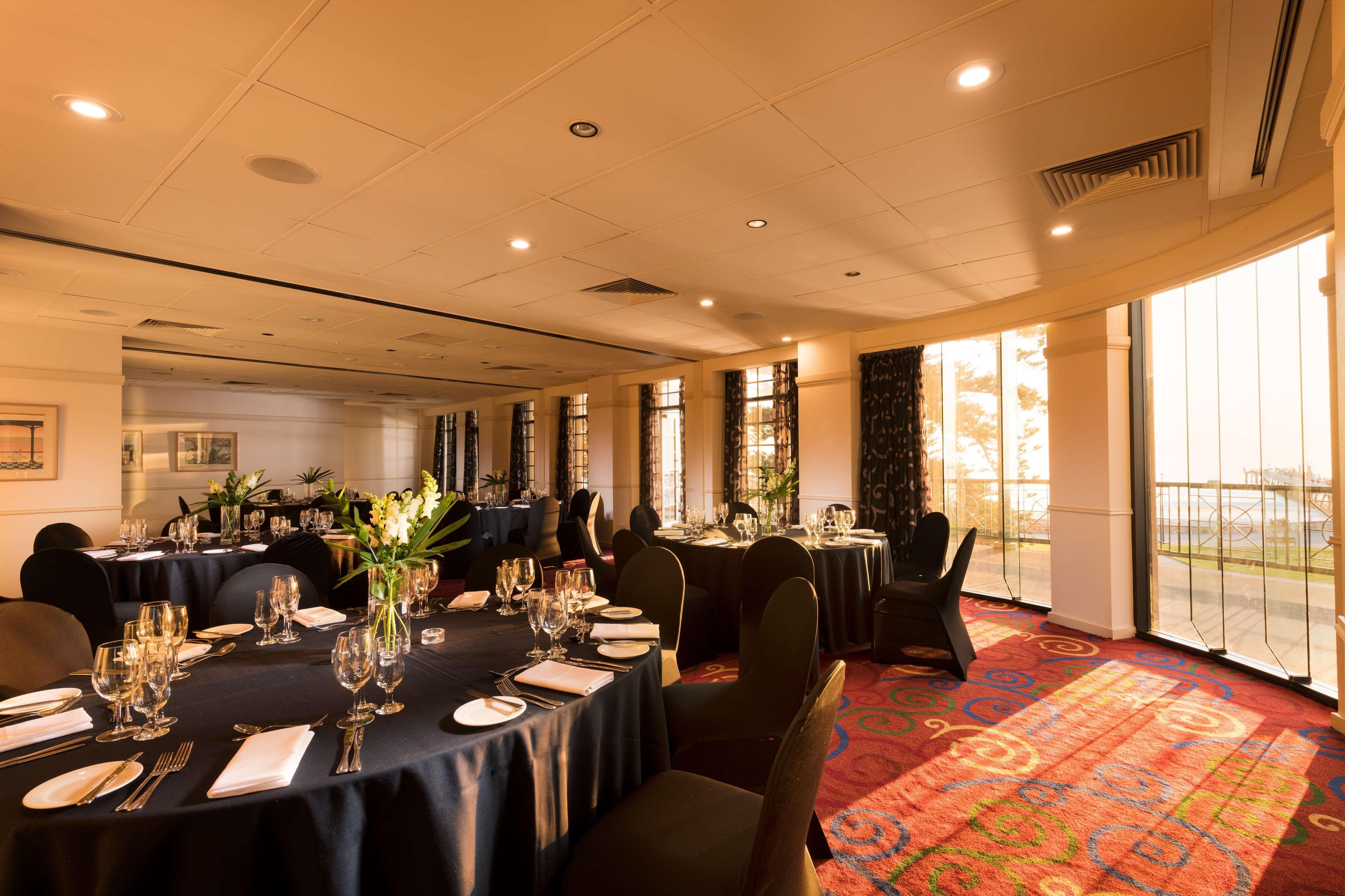 Stamford Grand Adelaide Otel Glenelg Dış mekan fotoğraf The photo shows a well-decorated event space or dining area. There are several round tables draped in dark tablecloths, each set with elegant dinnerware, including glasses and cutlery. The room features large windows that allow natural light to flood