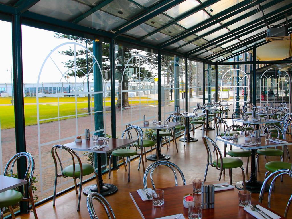 Stamford Grand Adelaide Otel Glenelg Dış mekan fotoğraf The photo shows the interior of a restaurant with a modern design. The space features several tables with green chairs, arranged in a way that allows for ample seating. Large glass windows provide a view of the outside, creating a bright and open atm