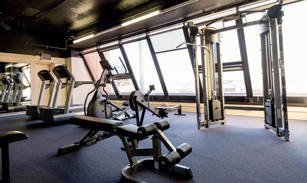 Stamford Grand Adelaide Otel Glenelg Dış mekan fotoğraf The photo shows a modern gym interior with several exercise machines. There are cardio machines, likely including treadmills and possibly an elliptical machine, along one side. In the center, there is a weight bench and a rowing machine. Additionally