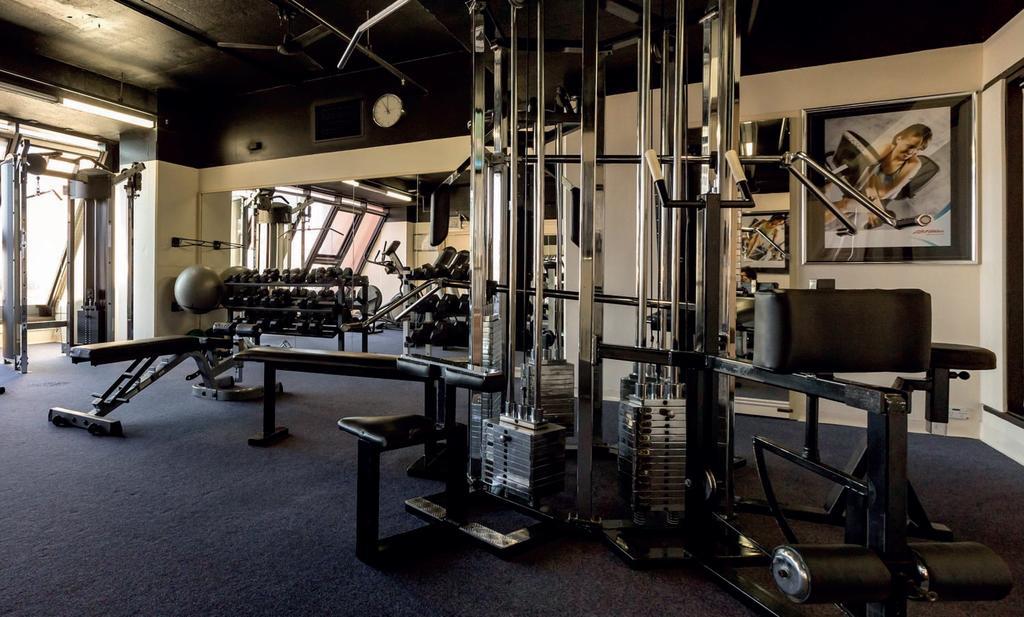 Stamford Grand Adelaide Otel Glenelg Dış mekan fotoğraf The photo shows a gym interior with several pieces of exercise equipment. In the foreground, there is a multi-station machine that features various pulleys and weights. To the side, there are benches and free weights, including dumbbells. The gym has